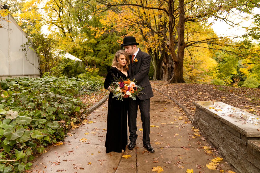 Bridal portraits from a Halloween Wedding in Highland Park. The bride is wearing a flowing black dress, and the groom is wearing a dapper suit with a top hat. The bride's wedding bouquet is a beautiful fall palette of white, rust, and dark purples. 