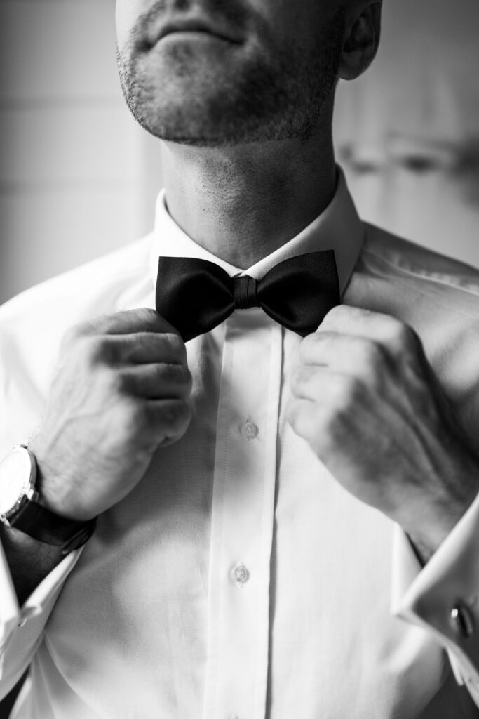 A timeless black and white wedding photo of the groom, captured in a classic pose that exudes elegance and romance. The image showcases the groom getting ready in crisp detail in a sharp suit. The editing style in the photo gives it a timeless quality, ensuring that it will remain beautiful and relevant for generations to come.
