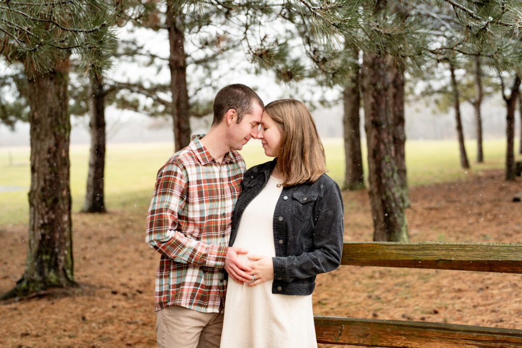A young couple is celebrating adding a new family member with a Rochester maternity session. The photos are romantic with snow falling around the couple surrounded in nature. 