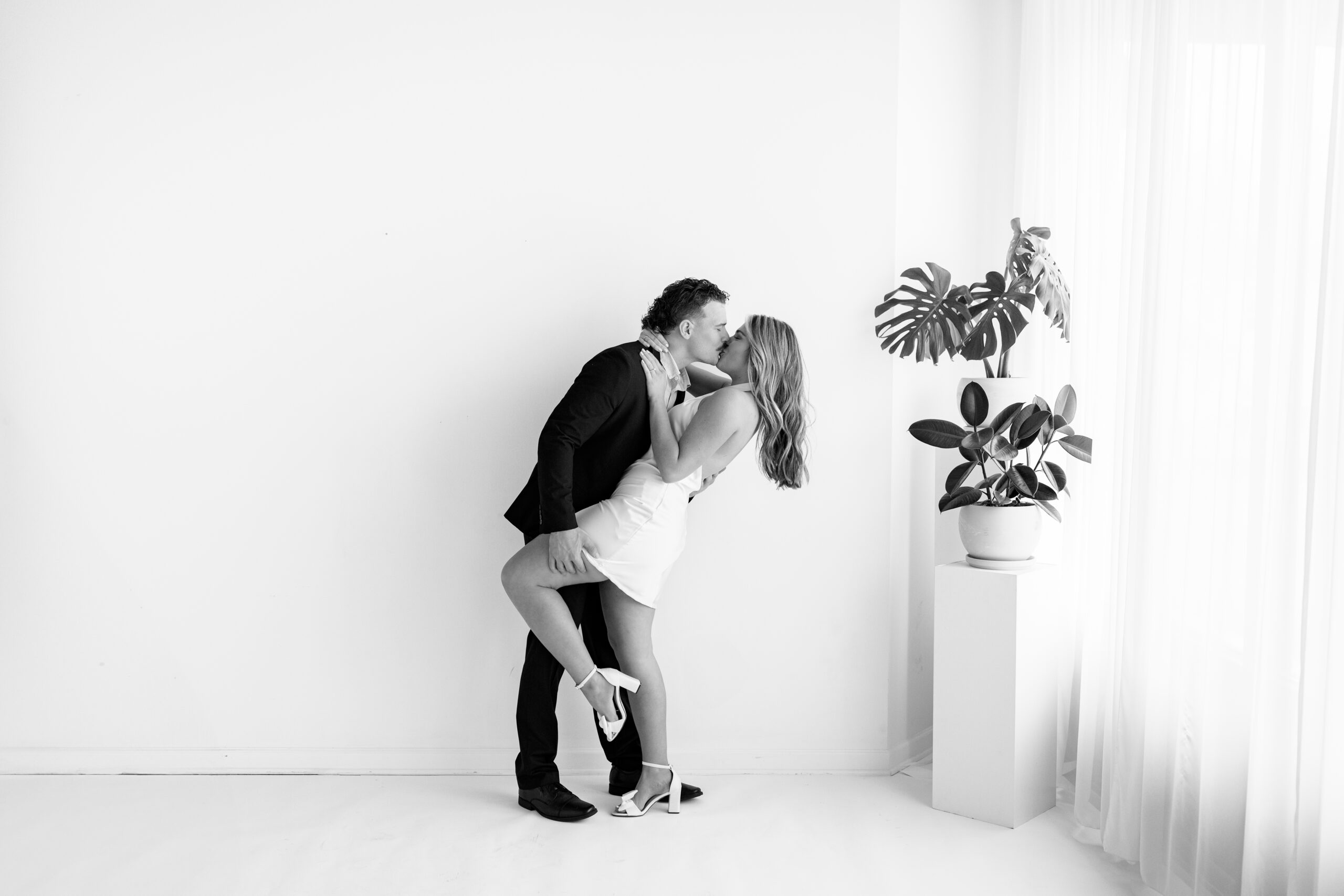 This photo depicts a modern, yet timeless engagement session at Gallery 48. This session features a couple named Jill and Ray, and they wore a formal outfit. They are pictured in an all white studio.